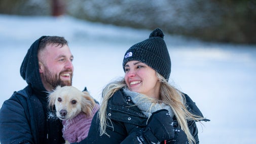 Two people are playing in the snow with their small dog at Lyme, Cheshire